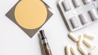 A nicotine patch, vape pen, and nicotine replacement therapy tablets arranged on a white surface.